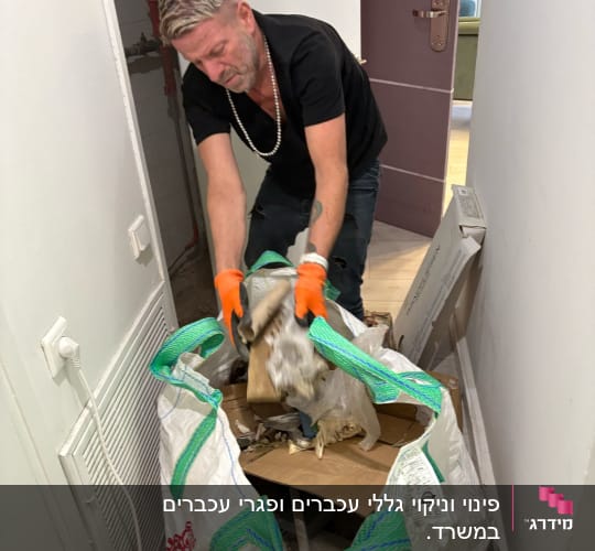 אדם עם כפפות כתומות מפנה שקית פסולת במסדרון